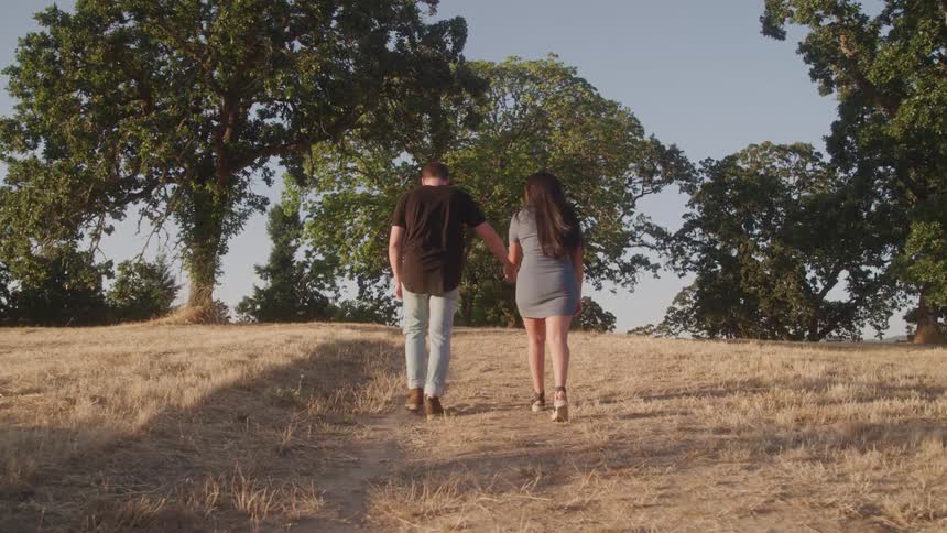 Couple holding hands walking through a dry grassy field