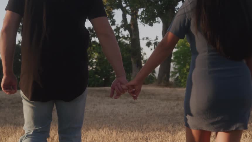 Two people are walking in nature while holding hands