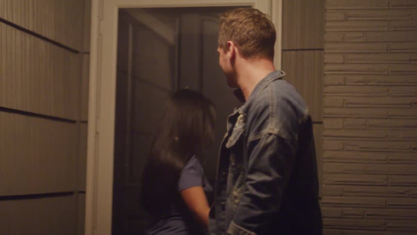 A man and a woman hug in the doorway of a home and the woman smiles at him before he turns to leave and she closes the door