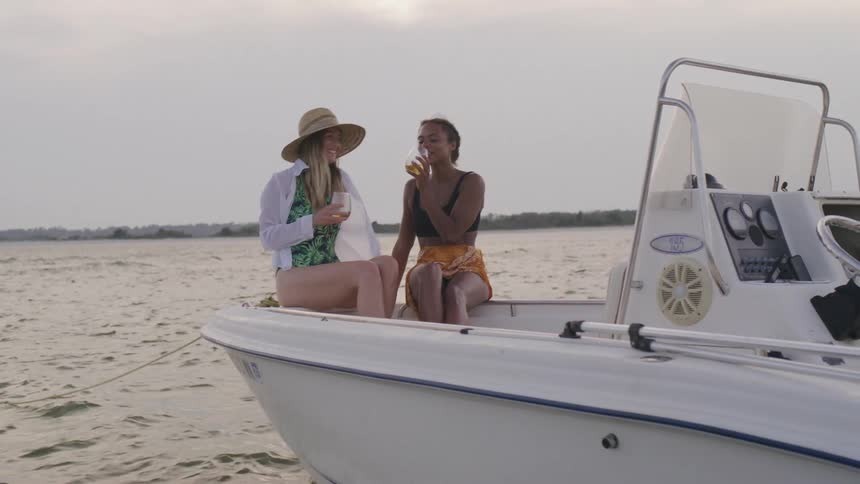 Two women on a boat have a glass of drink while on vacation in the ocean at midday