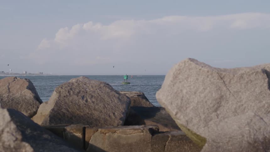 Rocks by the seashore frame the view of a green buoy floating in the ocean