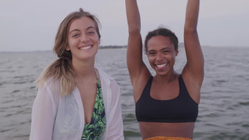 Two women smile and pose on a moving boat at sunset