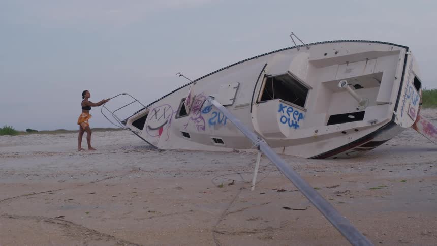Woman walks beside a capsized and graffitied boat on the sand