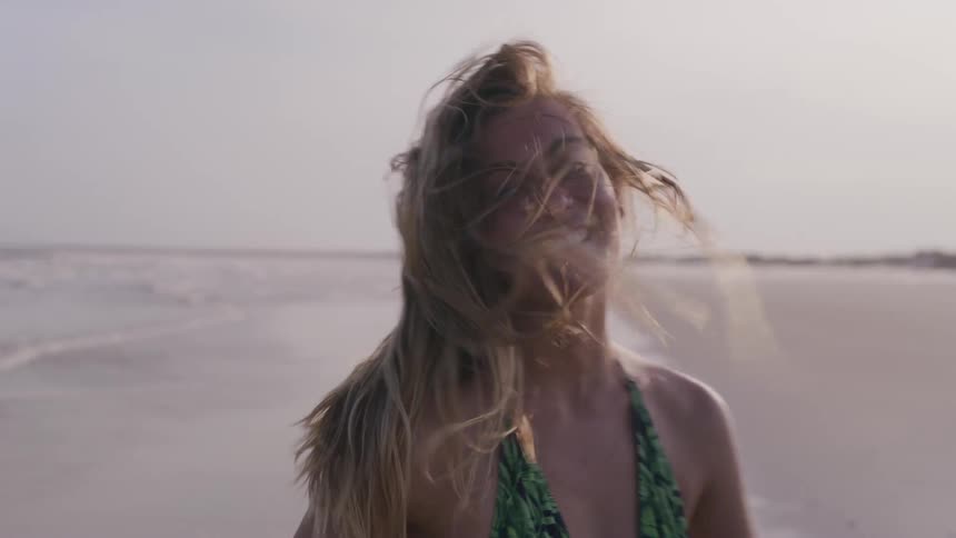Woman in a patterned swimsuit smiles at the beach with wind in her hair
