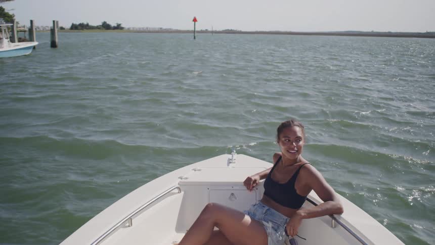 A woman relaxes on the bow of a boat under clear skies on open water
