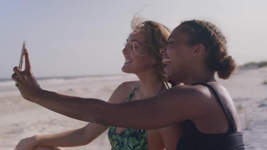 Two women smile and take a selfie on a sunny beach