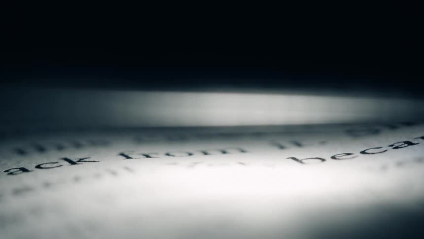 A closeup of printed text on a page is dramatically lit focusing on words