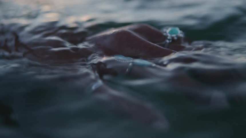 Hand adorned with blue stone rings emerges from the water