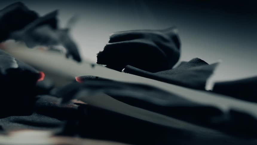 A closeup shows curled charred paper edges still glowing faintly with heat in a darkened setting