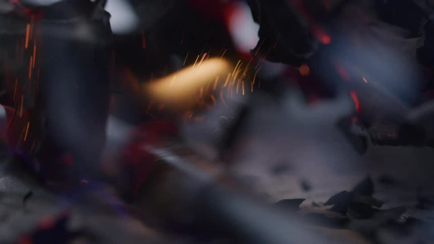 A burning paper curls at the edges revealing smoldering text amid glowing embers after a silver lighter ignites the paper