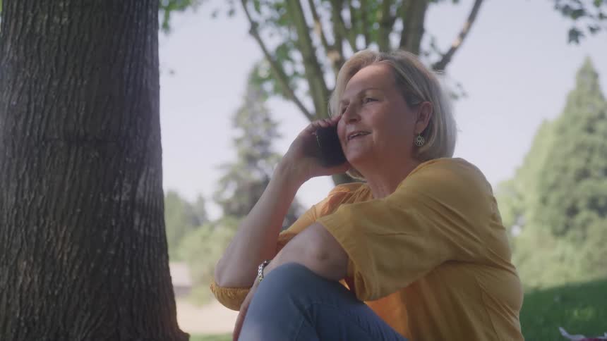 Woman sits under a tree talking on the phone in nature