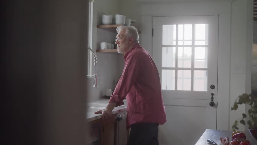 A man stands alone at kitchen sink gazing out window