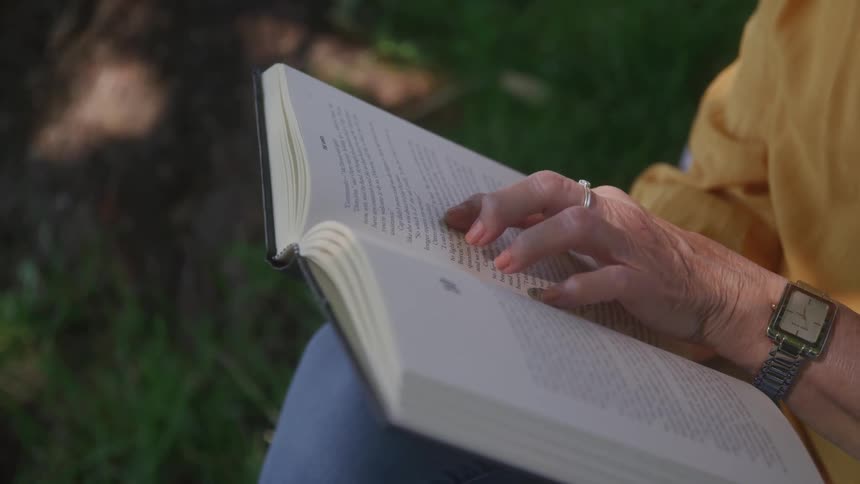 Closeup of hands holding and reading a book outdoors in natural light