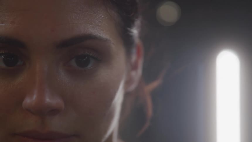 A determined sweaty woman stares ahead with intense focus in a dimly lit space