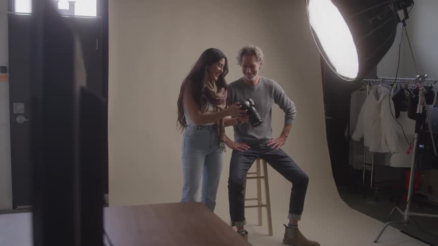 A man and a woman review photos together in a photography studio lit by a large softbox