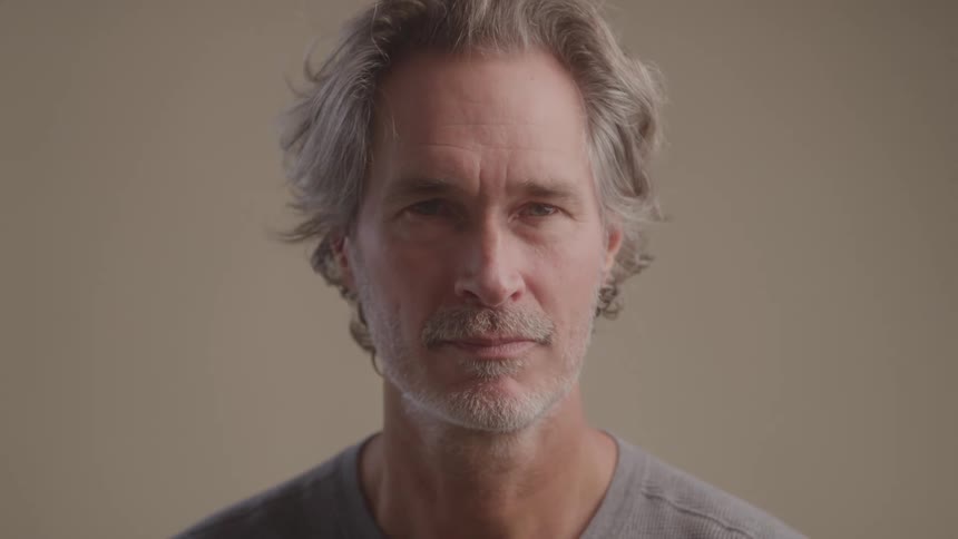 A close up shot captures a middle aged man with graying hair as he turns from a profile view to look directly at the camera