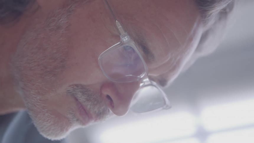 A closeup shot of a mans face focusing on his graying beard and nose he is wearing clearframed glasses and looking down with a thoughtful or focused expression