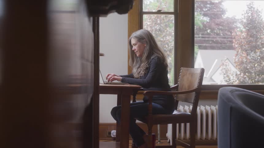 A woman sits alone using a laptop in a bright room