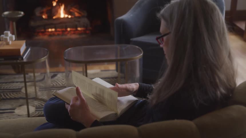 A woman reads in a cozy living room by the fireplace