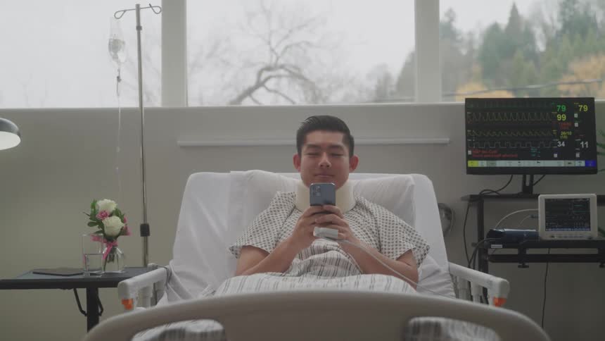 A man sits in a hospital bed using a smartphone