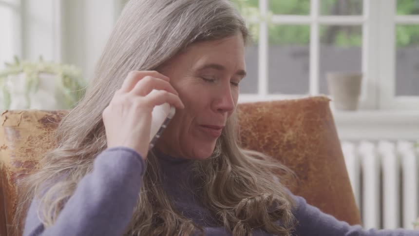 Portrait of a woman making a phone call while seated on a chair in a living room during daytime