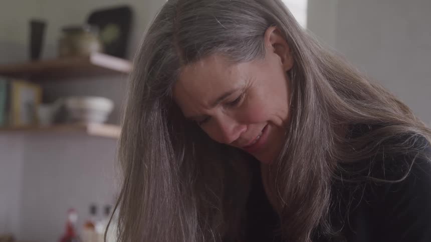 A woman smiles gently while looking down in a cozy kitchen setting