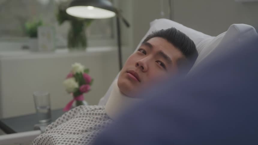 A man with a neck brace wakes up in a hospital bed looking around the room