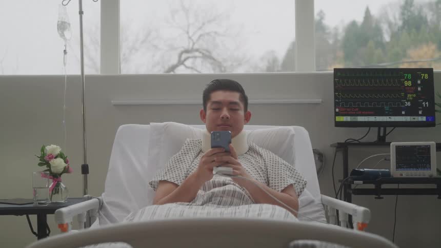 Patient with a neck brace uses a cellphone in a hospital bed
