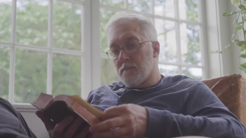An older man sitting on a sofa reading a book
