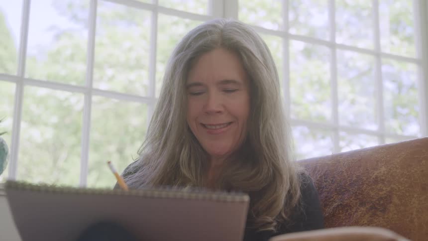 Woman with happy expression sitting down drawing in a notebook