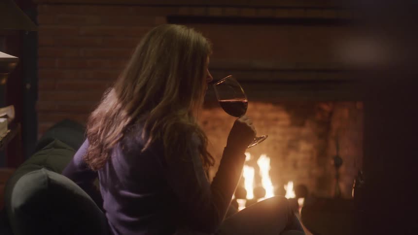 Woman relaxes with red wine in front of a fireplace