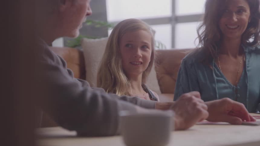 A family of threefather mother and daughtersits in the dining area playing a card game and having fun
