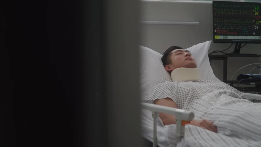 A man lays in a hospital bed asleep with a neck brace around his neck