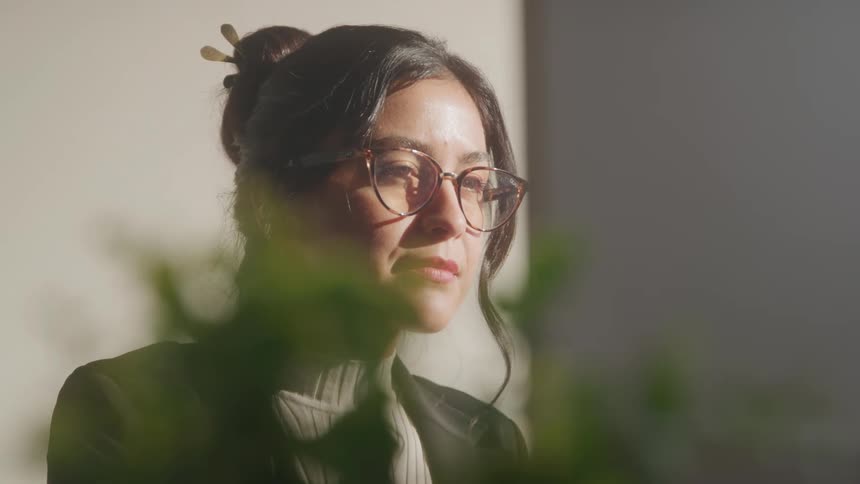 Woman holds her glasses while observing something with a focused expression