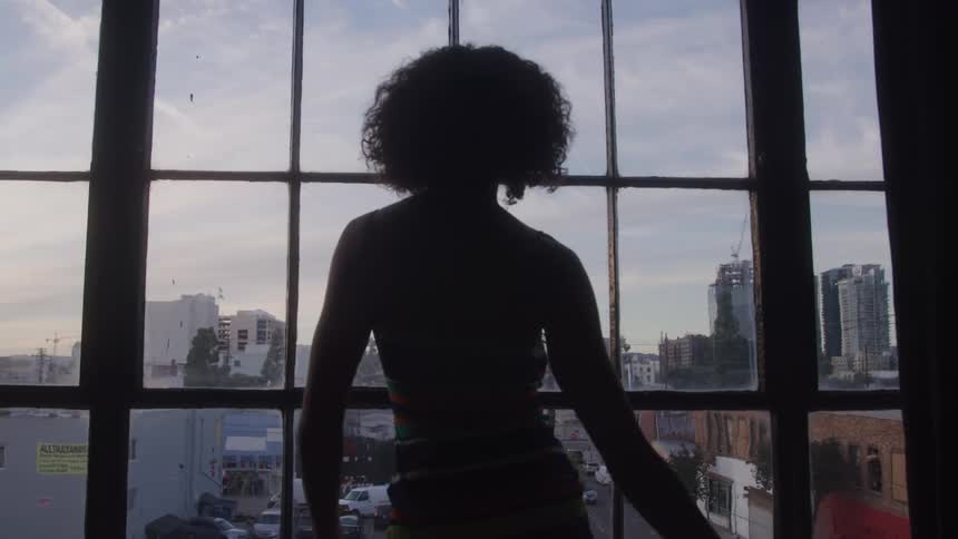 Silhouette of a woman dancing in front of a large window at dusk
