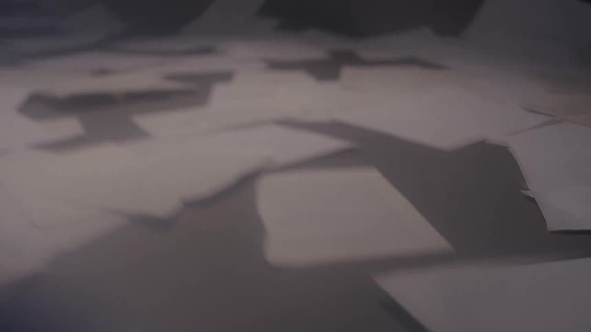 Sheets of paper scattered across the floor among others still falling