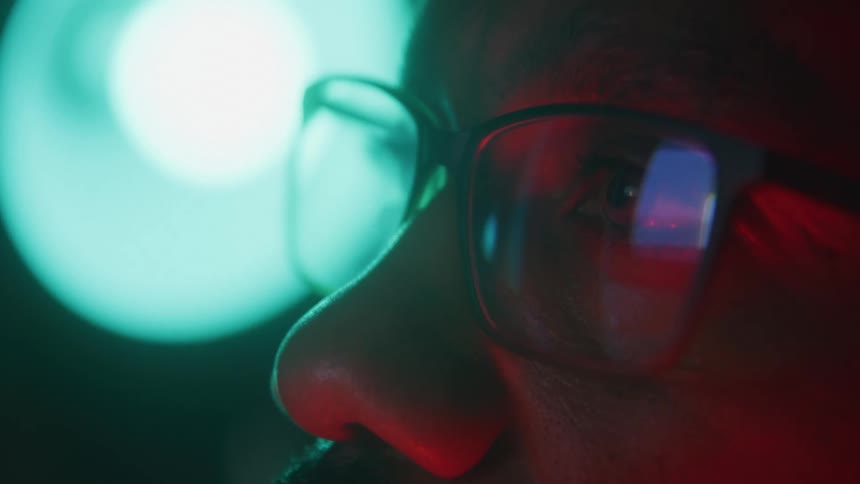 Closeup face shows focused eyes behind glasses lit by colored light