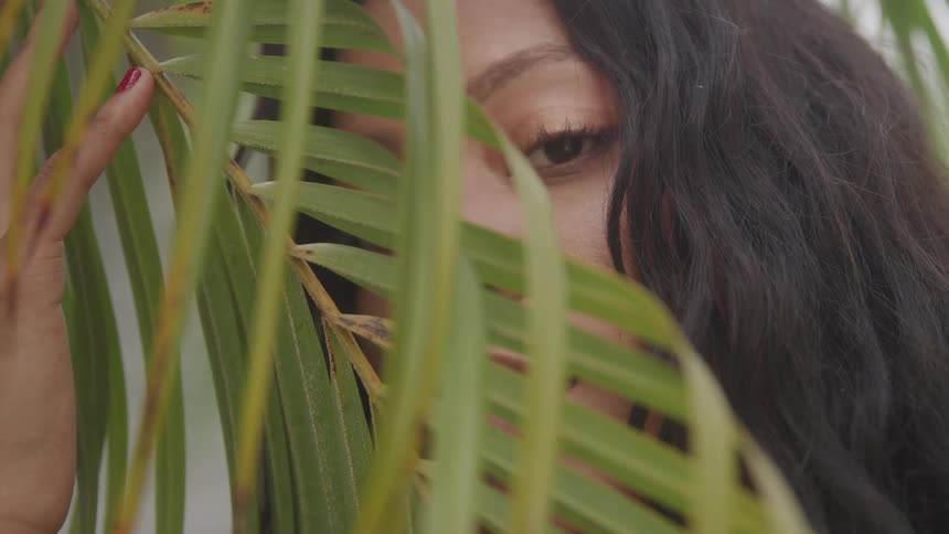 Woman looks through palm leaves while holding the branch