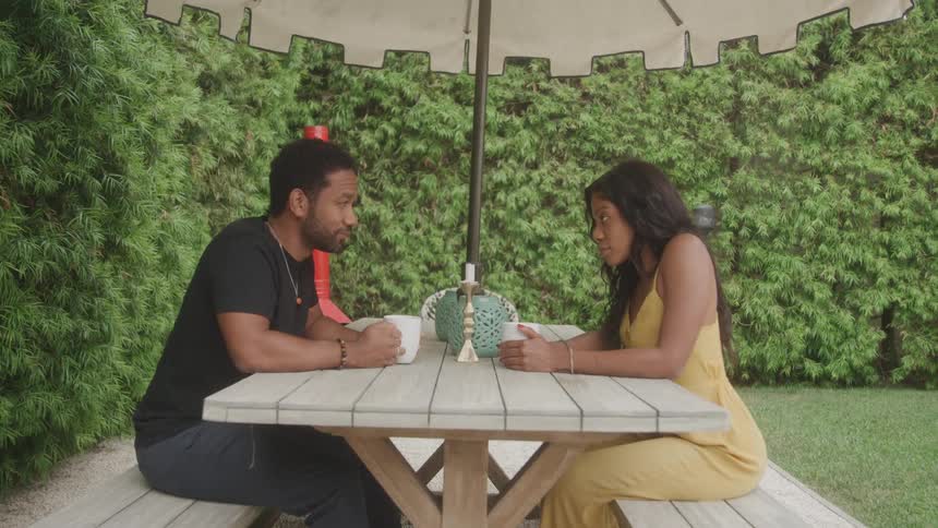 Couple chats smiling while seated at a wooden table outdoors