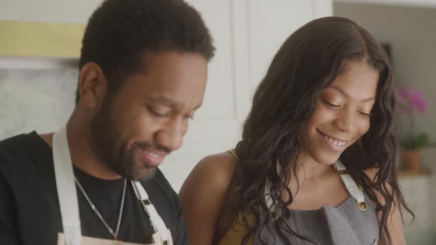 Smiling couple wearing aprons shares a moment together in the kitchen