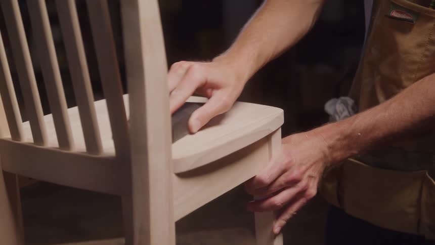Man carefully sands a wooden chair with a sanding block