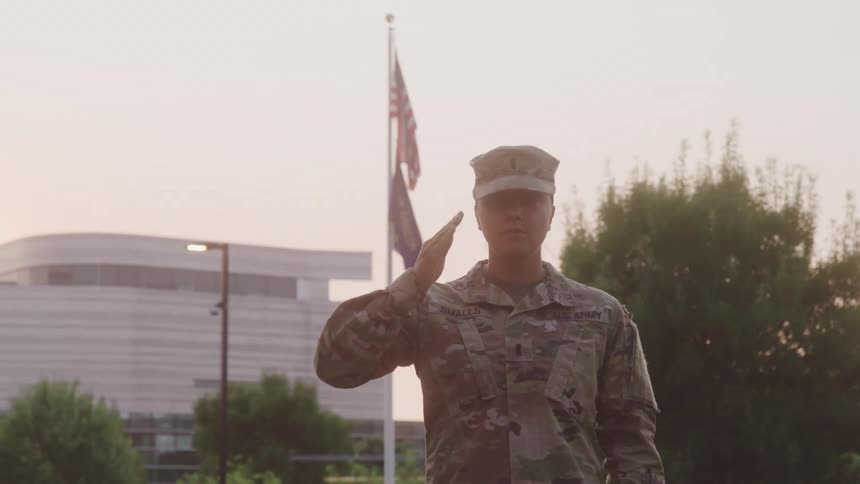 Soldier in camouflage uniform salutes in front of an american flag