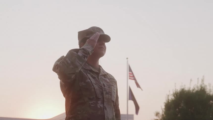 Woman in military uniform salutes with the flag in the background