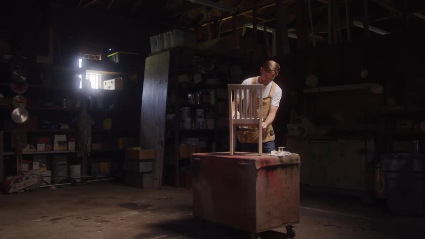 Man works sanding or adjusting a wooden chair inside a workshop