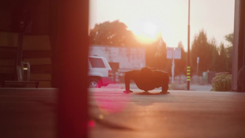 Person does pushups on the floor of a warehouse with the sunset in the background