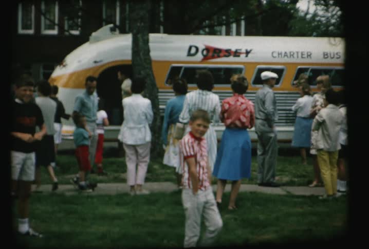An older film of people standing around looking at an old bus