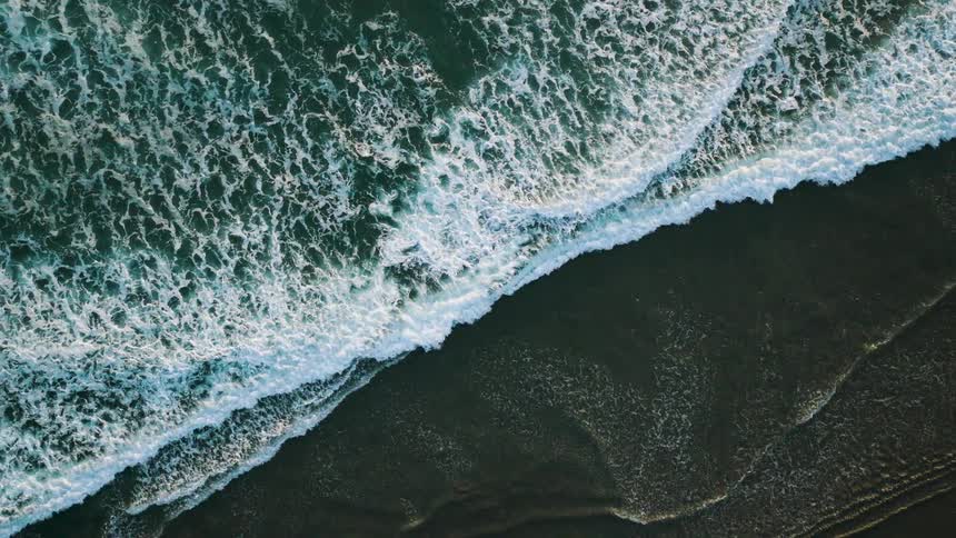 Aerial of sea waves flowing up against the sea shore during daytime