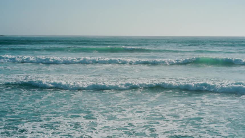 Ocean waves crash against the beach at midday