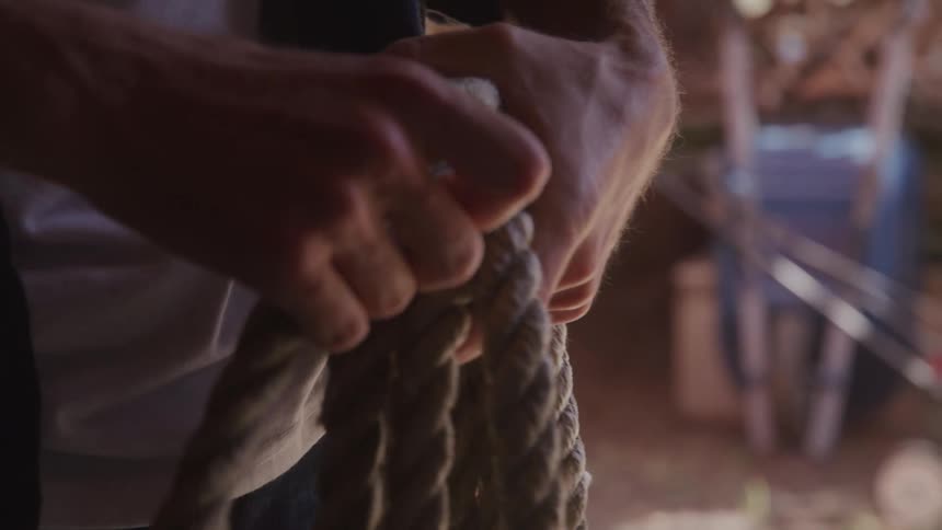 A person is seen in a closeup working with a rope in their hands the rope is thick and appears to be made of natural fibers