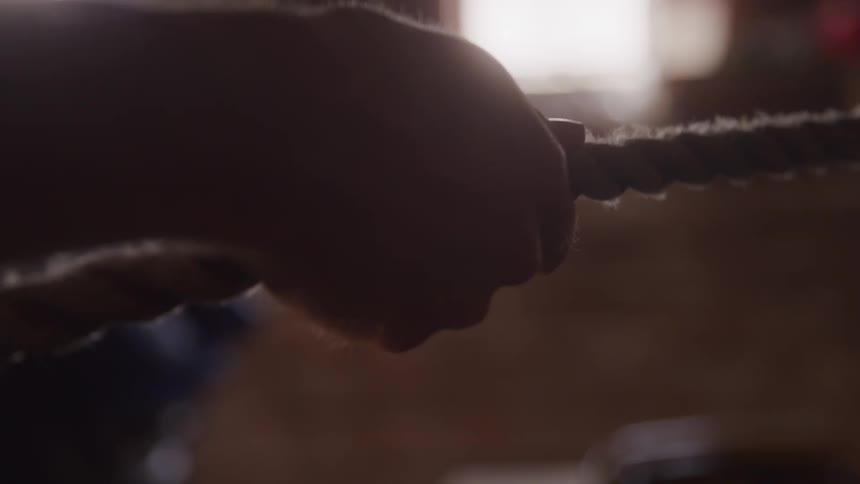 A mans hand grips a thick rough rope with a blurry sunlit background
